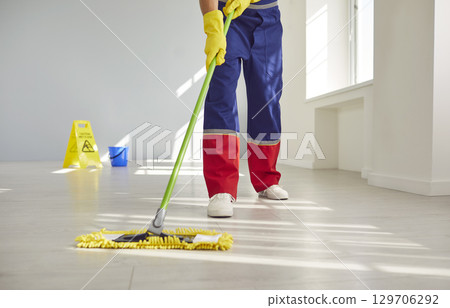 Low angle cropped photo of male janitor legs cleaning floor with mop indoors. Low angle cropped photo of male janitor legs cleaning floor with mop indoors. 129706292