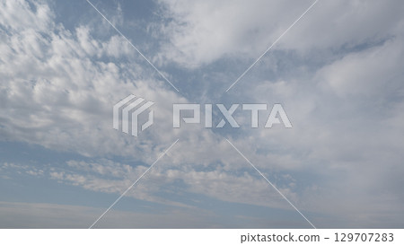 Blue sky with scattered white cirrus clouds. The clouds vary in size and shape, creating a serene atmosphere. Background light blue. 129707283