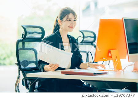 操作一台個人計算機的一個年輕女商人在辦公室 操作一台個人計算機的一個年輕女商人在辦公室 129707377