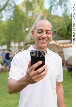 Happy bald man relaxing at campsite with camper van in outdoor travel lifestyle scene using phone Happy bald man relaxing at campsite with camper van in outdoor travel lifestyle scene using phone 129708232