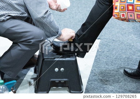 Man polishing another man's shoe while seated on a stool in a well-lit indoor setting Man polishing another man's shoe while seated on a stool in a well-lit indoor setting 129708265