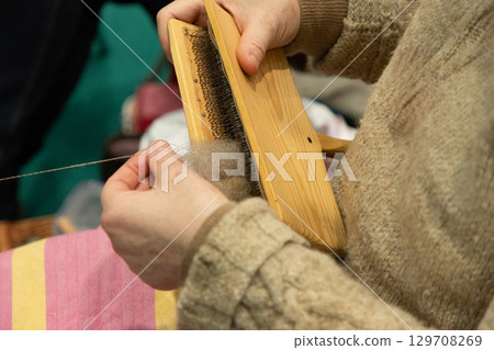 Hands of a person using a wooden carder to prepare wool fibers for spinning into yarn 129708269
