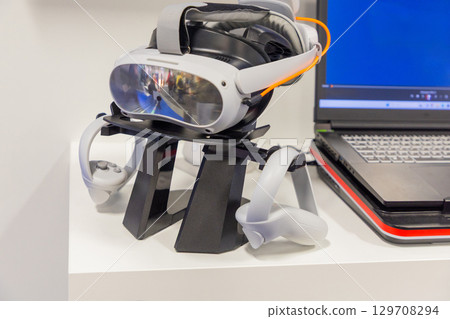 Virtual reality headset mock up displayed on a stand beside a laptop with a blue screen 129708294