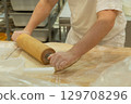Baker rolling dough on wooden surface in a professional kitchen with flour scattered around 129708296