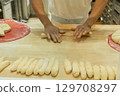 Baker shaping dough into rolls on wooden countertop in a professional kitchen environment 129708297