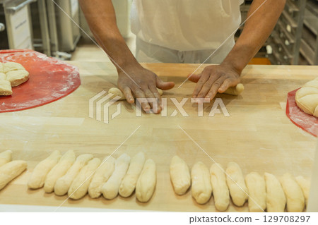 Baker shaping dough into rolls on wooden countertop in a professional kitchen environment Baker shaping dough into rolls on wooden countertop in a professional kitchen environment 129708297