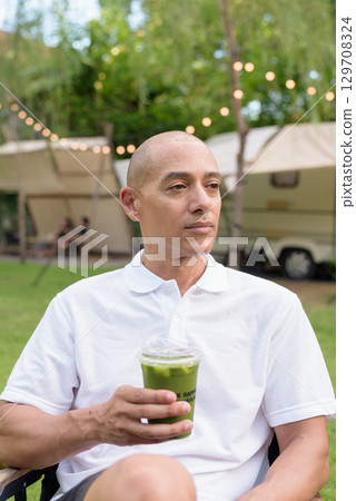Confident bald man relaxing at campsite with camper van having healthy green detox juice drink 129708324