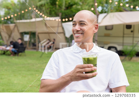 Confident bald man relaxing at campsite with camper van having healthy green detox juice drink 129708335