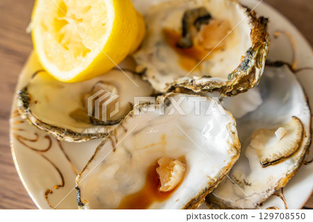 Empty oyster shells with lemon remains and sauce traces on a kitchen surface. Scene after eating seafood at home. Empty oyster shells with lemon remains and sauce traces on a kitchen surface. Scene after eating seafood at home. 129708550