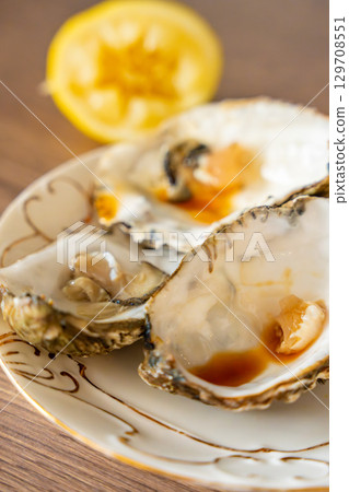 Empty oyster shells with lemon remains and sauce traces on a kitchen surface. Scene after eating seafood at home. Empty oyster shells with lemon remains and sauce traces on a kitchen surface. Scene after eating seafood at home. 129708551