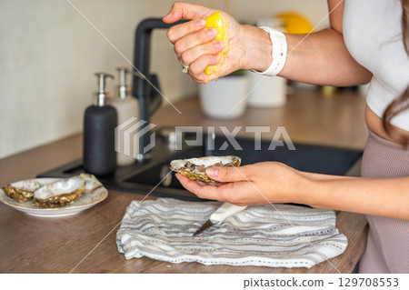 Freshly opened oyster held in hands and sprinkled with lemon juice. Homemade seafood preparation before eating 129708553
