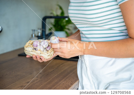 Hands of young woman holding a basket with Chinese single clove garlic on the kitchen table. Organic cooking ingredient, natural food, and culinary preparation. Hands of young woman holding a basket with Chinese single clove garlic on the kitchen table. Organic cooking ingredient, natural food, and culinary preparation. 129708568
