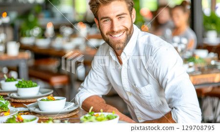 Smiling man in a casual shirt enjoying healthy salad in a vibrant restaurant setting 129708795