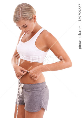 Fitness, health and woman with tape measure for abdomen in studio isolated on a white background. Diet, wellness and slim female model measuring waist to track weightloss goals, progress or targets. 129709227