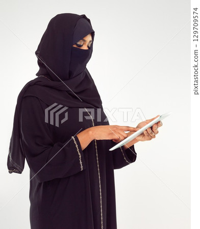 Woman, tablet and hijab of muslim for online islamic research against a white studio background. Female standing holding touchscreen with scarf reading news on islam, arabic or culture 129709574