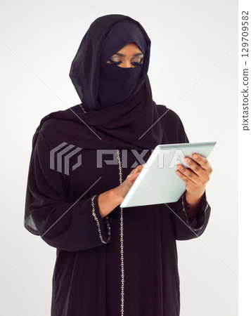 Woman, tablet and muslim typing with hijab for online islamic research against grey studio background. Female isolated standing holding touchscreen with scarf reading news on islam, arabic or culture 129709582