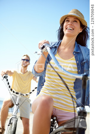 Cycling, travel and couple with a woman on summer vacation or holiday riding on the promenade by the beach. Bike, freedom and date with a girlfriend outdoor for a ride on the coast during the day 129709848