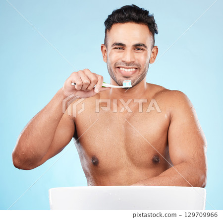 Toothbrush, toothpaste and indian man portrait brushing teeth in blue background studio for hygiene wellness, cleaning or dental healthcare. Face, happy and smile for morning dental care routine Toothbrush, toothpaste and indian man portrait brushing teeth in blue background studio for hygiene wellness, cleaning or dental healthcare. Face, happy and smile for morning dental care routine 129709966