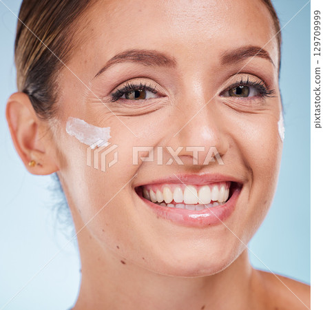 Skincare, beauty and portrait of a woman with face cream for health, wellness and natural face routine. Cosmetic, happy and model with facial lotion, spf or creme isolated by a blue studio background 129709999