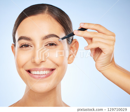 Beauty, tweezers and portrait of woman on blue background, facial grooming and professional hair removal. Spa, salon and skincare, happy woman plucking or tweezing eyebrows hair. Beauty, tweezers and portrait of woman on blue background, facial grooming and professional hair removal. Spa, salon and skincare, happy woman plucking or tweezing eyebrows hair. 129710029