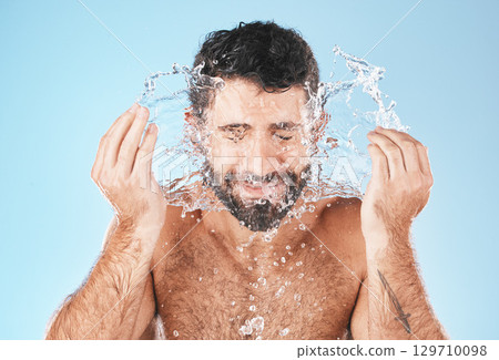 Face, splash and man in studio for cleaning, wellness and personal health with self care by blue background. Model, facial and healthy with water splash, skincare and cosmetics by studio backdrop 129710098