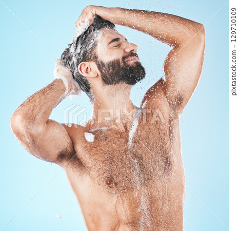 Haircare, keratin and cleaning with a man in studio on a blue background to take a shower for hygiene. Water, skin and relax with a male washing his hair with shampoo treatment in the bathroom 129710109