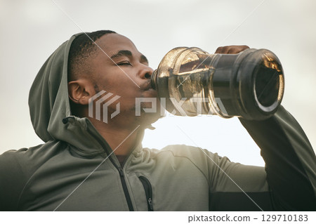 Fitness, health or black man drinking water after training, exercise or workout for body hydration. Thirsty runner, bottle or tired sports athlete relaxing with goals or motivation resting in Chicago 129710183
