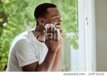 Beard, cream and shaving black man in the morning, beauty grooming and hair removal in a home bathroom. Skincare, cosmetic and happy African person applying foam to face for clean facial hair shave 129710222