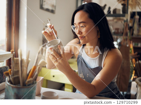 Asian woman, clay studio and painting design of ceramic sculpture product, creative manufacturing and workshop. Painter, pottery artist and brush mug, pattern process and production in small business 129710299
