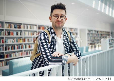 College, portrait and man student in a bookstore for studying, learning or knowledge with books. Education, library and young male with a college scholarship standing in the academic study area. College, portrait and man student in a bookstore for studying, learning or knowledge with books. Education, library and young male with a college scholarship standing in the academic study area. 129710311