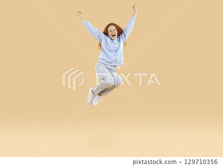 Overjoyed excited teenage girl who feels euphoria joyfully shouts and jumps high with raised arms. Overjoyed excited teenage girl who feels euphoria joyfully shouts and jumps high with raised arms. 129710356