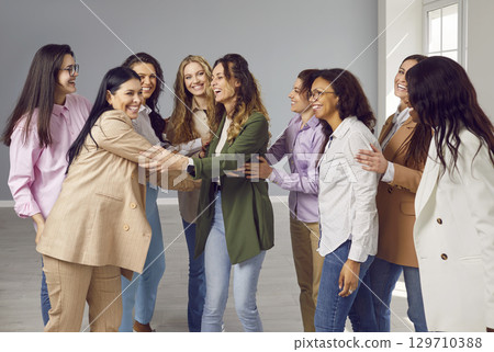 Happy cheerfull young diverse women friends or coworkers hugging and laughing on grey background. Happy cheerfull young diverse women friends or coworkers hugging and laughing on grey background. 129710388