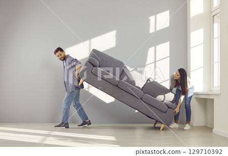Happy young couple carrying sofa to their new home 129710392