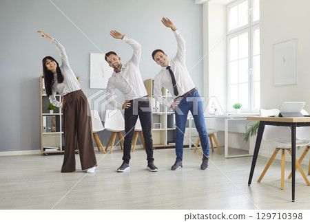 Smiling coworkers doing side bends together during a light office stretch break 129710398