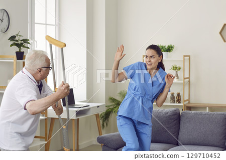 Angry elderly patient showing aggression and fighting medical nurse with his crutch 129710452