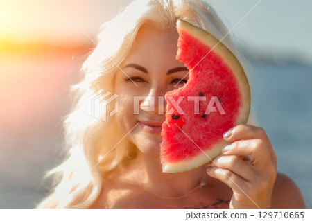 Woman Watermelon Beach Summer: Outdoors portrait, blonde woman playfully holding a bitten watermelon slice near sea, sunny day. Woman Watermelon Beach Summer: Outdoors portrait, blonde woman playfully holding a bitten watermelon slice near sea, sunny day. 129710665