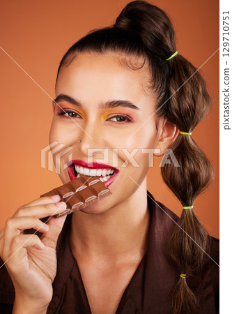 Chocolate, beauty and portrait girl eating sugar candy, sweets or dark chocolate dessert for stress relief. Skincare, facial cosmetics makeup and model woman face with cacao product for antioxidants 129710751