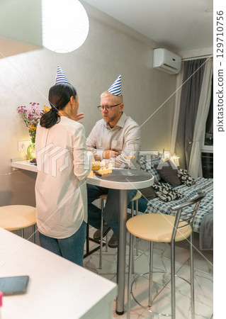 Couple Birthday Apartment Celebration: Mature couple celebrates birthday at home, intimate setting, enjoying cake. Couple Birthday Apartment Celebration: Mature couple celebrates birthday at home, intimate setting, enjoying cake. 129710756