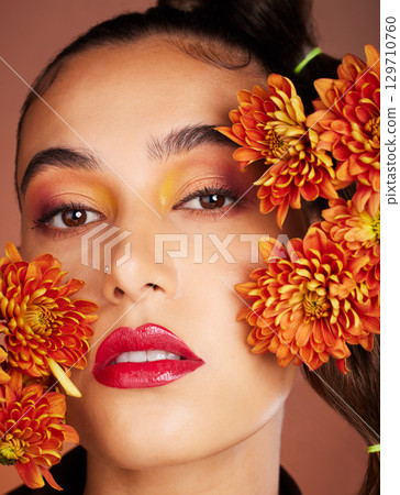 Makeup, beauty or woman in studio with flowers for art fashion and natural facial cosmetics for self care. Face portrait, orange plants or girl model with red lipstick, eyeshadow and glowing skin Makeup, beauty or woman in studio with flowers for art fashion and natural facial cosmetics for self care. Face portrait, orange plants or girl model with red lipstick, eyeshadow and glowing skin 129710760