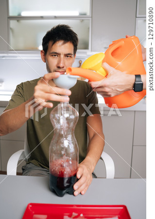 Vertical cropped shot of two biology students preparing fertilizer solution with watering can, funnel and plastic bottles in lab, showcasing approach to botanical research. Concept of urban farming. 129710890