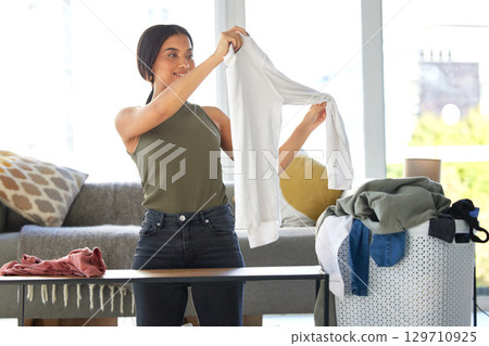 Housework, cleaning and woman folding laundry, organizing clothes and clean washing in living room. Smile, basket and housekeeping cleaner with clothing to fold during morning routine in the lounge 129710925