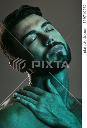 Man, face and neon with beauty and skincare, grooming and wellness with eyes closed against studio background. Healthy skin, relax in blue light and peace, male and cosmetic facial and treatment 129710982