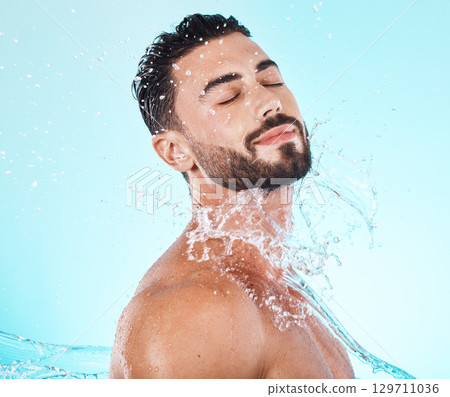 Water, splash and skincare with face of man for shower, self care and natural cosmetics. Luxury, hydration and refreshing with model for dermatology, wellness and cleaning in blue background studio Water, splash and skincare with face of man for shower, self care and natural cosmetics. Luxury, hydration and refreshing with model for dermatology, wellness and cleaning in blue background studio 129711036