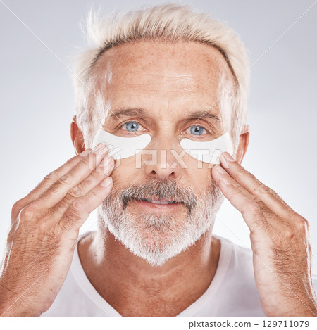 Senior man with collagen eyes mask in skincare, dermatology facial and face cosmetics advertising in studio portrait. Elderly model with hands application of eye patch, anti aging product and beauty Senior man with collagen eyes mask in skincare, dermatology facial and face cosmetics advertising in studio portrait. Elderly model with hands application of eye patch, anti aging product and beauty 129711079