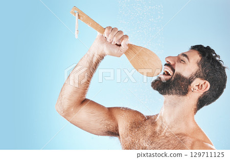 Bathroom, singing and washing with a man model in studio on a blue background using a loofah to sing. Water, showering and hygiene with a handsome male wet while cleaning for personal body care Bathroom, singing and washing with a man model in studio on a blue background using a loofah to sing. Water, showering and hygiene with a handsome male wet while cleaning for personal body care 129711125
