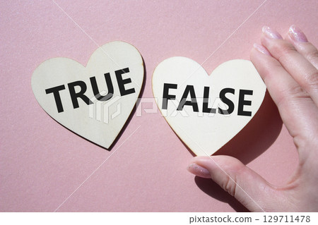 True or False symbol. Concept word True or False on wooden hearts. Businessman hand. Beautiful pink background. Business and True or False concept. Copy space 129711478