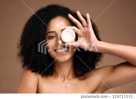 Face, product and skincare with a model black woman in studio on a brown background for skin treatment. Portrait, container and beauty with an attractive young female posing to promote antiaging care 129711531
