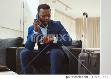 African businessman, checking time in hotel and phonecall for work travel schedule in Atlanta. Young black entrepreneur speaking on cellphone, professional time management or luxury airport travel 129711635