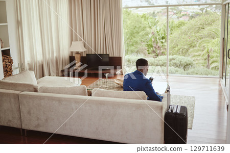 Phone, travel and hospitality with a business black man sitting on a sofa in the living room of a hotel with his luggage. Back, bag and communication with a male employee typing a text message Phone, travel and hospitality with a business black man sitting on a sofa in the living room of a hotel with his luggage. Back, bag and communication with a male employee typing a text message 129711639