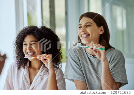 Oral care, toothbrush and female friends with a hygiene, health and wellness morning routine. Happy, smile and interracial women doing a dental treatment while brushing teeth in the bathroom. 129711683